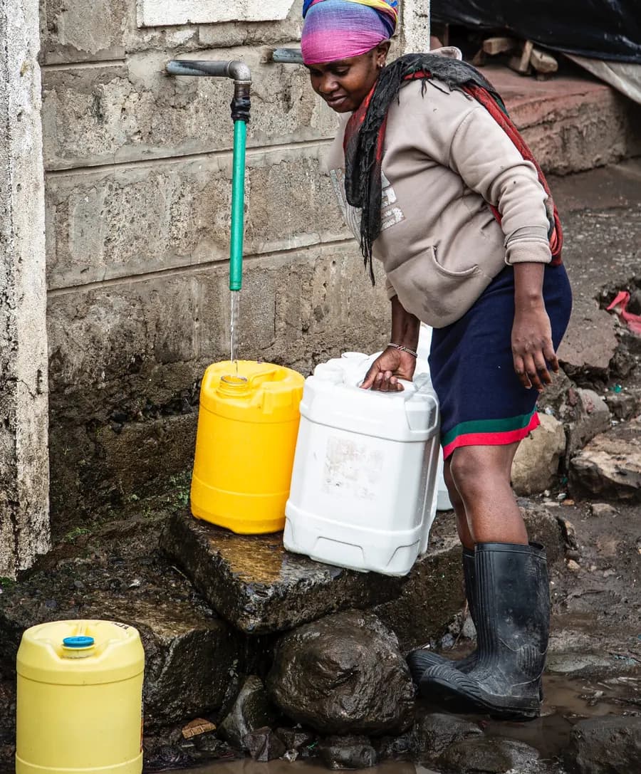 Eine Frau füllt an einer Wasserstelle in Korogocho gelbe und weiße Kanister.